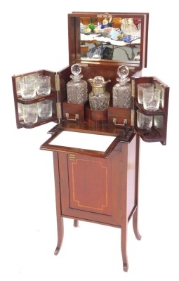 An Edwardian mahogany drinks cabinet, the hinged inlaid top with a moulded edge opening to reveal three recesses containing three cut glass decanters with lower drawer to each section, mirror to underside of lid, two hinged doors to front of cabinet conta