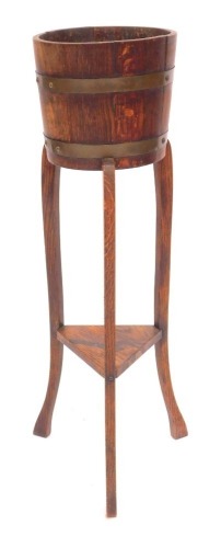 An early 20thC oak plant stand, the circular top with cooper banding, on square outswept legs united by an under tier, 90cm high.