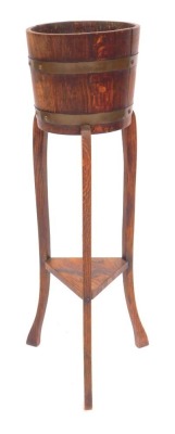 An early 20thC oak plant stand, the circular top with cooper banding, on square outswept legs united by an under tier, 90cm high.