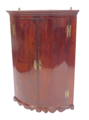 A George III mahogany bow front corner cabinet, two doors enclosing an arrangement of shelves, shaped base, 102cm high, 75cm wide, 47cm deep.