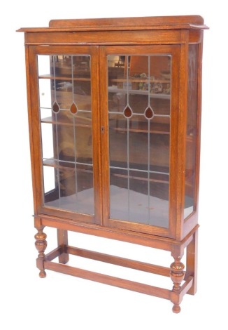 An early 20thC oak display cabinet, the top with a raised back, above two leaded glazed doors enclosing four shelves, on turned legs, united by stretchers, 143cm high, 87cm wide, 25cm deep.