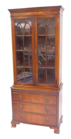 A 20thC mahogany display cabinet in Regency style, the top with dentil moulding above two glazed arched panelled doors enclosing an arrangement of shelves, the base with a slide drawer above three drawers with lion mask ring handles, on ogee bracket feet,