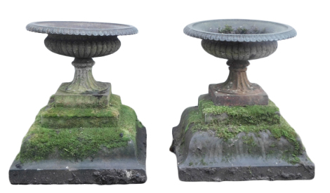 A pair of cast metal garden urns, each of cylindrical form, with lappet border, on a stepped stone base, 51cm high.