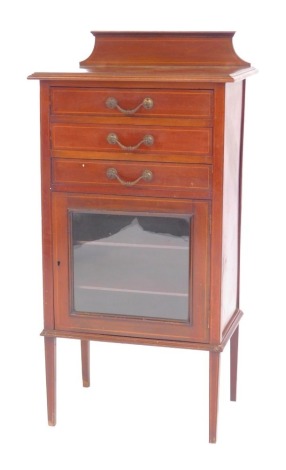 An Edwardian mahogany and line inlaid music cabinet, the top with a raised back with a moulded edge, with three drawers, the base with a cupboard glass inset panel enclosing two shelves, on square tapering legs, 109cm high, 54cm wide, 37cm deep.