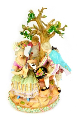 A 20thC Meissen porcelain figure group, of an 18thC gallant, presenting flowers from within his hat, to a seated lady playing a small guitar, against a tree, with a boy behind, raised on a naturalistic and oval garlanded base, printed marks, 28.5cm high.