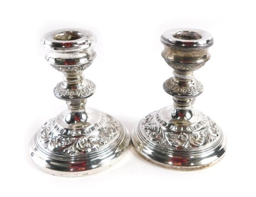 A pair of Elizabeth II silver squat candlesticks, with embossed rococo scroll design, on weighted bases, maker B&Co, Birmingham 1962, 11cm high.