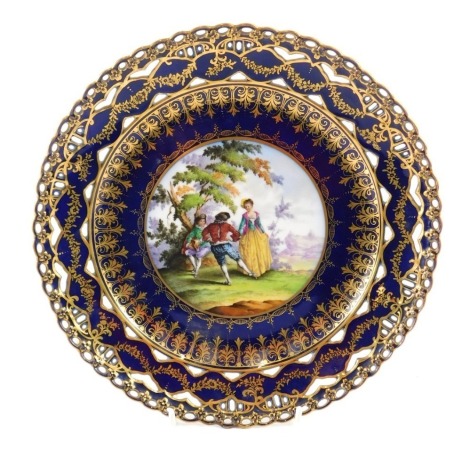 A Dresden porcelain plate, painted with figures, in 18thC scene within cobalt blue in gilt pierced borders, hand written Dresden mark and floral motif, decoration possibly later, 24cm diameter.