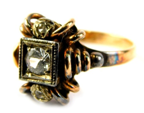 An abstract dress ring, with raised spiral design and a central square set with round brilliant cut diamond, approx 0.11ct, and two tiny diamond outer borders, on a yellow metal band stamped 750, with soldering colouration, ring size P½, 5.2g all in.