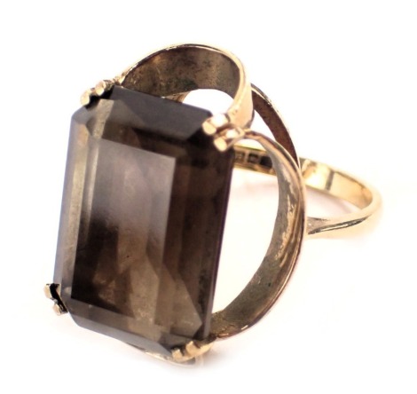 A 9ct gold smoky quartz dress ring, the rectangular cut smoky quartz in four double claw setting, in raised swirl shank, ring size N, yellow metal stamped 9ct, 6.6g all in.