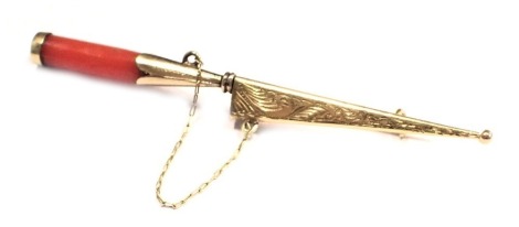 An dagger brooch, with a coral handle, in a yellow metal casing, the stainless steel blade stamped Corsa, unmarked, with safety chain and single pin back, 6cm wide, 3.2g all in.