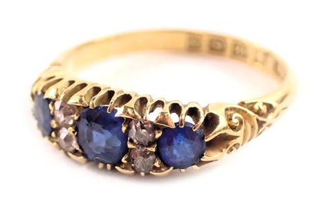 An 18ct gold sapphire and diamond gypsy ring, set with three oval sapphires, each in claw setting and broke by round brilliant cut diamonds, with scroll design shoulders, ring size R, Birmingham 1900, 4.3g all in.