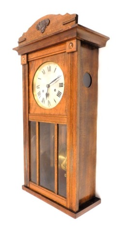 A 1950s/60s oak cased wall clock, with the arch pediment top above silvered Roman numeric dial, with three sectional glass panelled door, 30 hour movement, 68cm high, 32cm wide, 14cm deep.