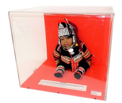 A costume doll model of a Northern Thai baby, wearing traditional costume of the Akha Hill Tribe in Northern Thailand, in perspex case, 51cm wide.