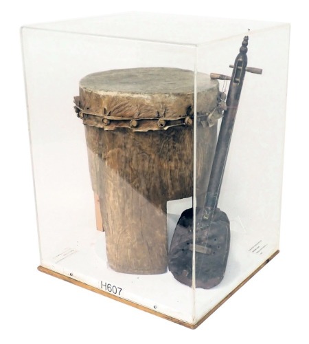 Tribal Art. An African drum with hide lid, and an African stringed instrument, both in same glazed and wooden case, 53cm high, 40cm wide.