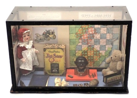 A display case showing toys from 1900-1935, to include a money box, jigsaw, etc., 64cm wide.