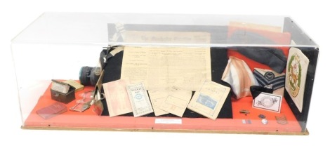 A display case containing various World War II memorabilia, to include newspapers, ephemera, RAF cap, badges, in perspex and wood case, 109cm wide.