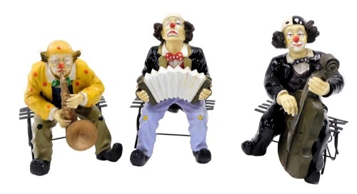 Three resin clown figures, each seated, comprising one playing trumpet, another cello, 25cm high. (3)