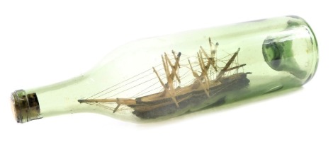 An early 20thC glass ship in a bottle, of cane three mast structure, on rocky supports with cork stopper, 30cm high.