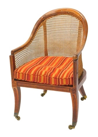 A Regency mahogany bergere library chair, with a moulded frame, caned back and sides, striped squab cushion, on sabre legs with brass castors. (AF)