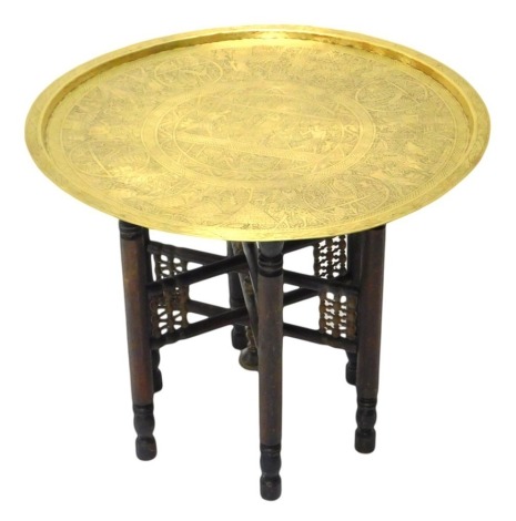 An Egyptian occasional table, the brass top engraved with hieroglyphic figures, on folding turned base, 68cm diameter.