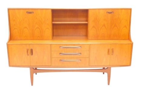 A 1970's teak sideboard, the raised top with a two fall-front doors, flanking a shelf the base with arrangement of three drawers, and two pairs of doors, on square tapering legs, 188cm wide.