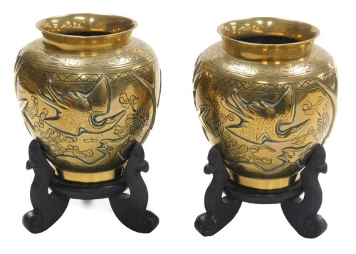 A pair of early 20thC Chinese heavy brass vases, embossed with a deer, bamboo, trees and a crane, the bases with seal script marks on wooden stands, 19.5cm high.