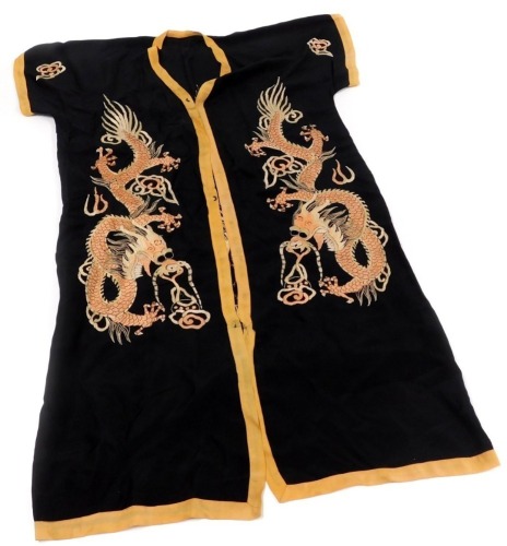 An early 20thC Chinese black silk short surcoat, embroidered with dragons in pink and white, with peach trim.