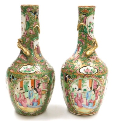 A pair of early 19thC Qing dynasty Cantonese famille rose porcelain vases, of long necked, ovoid form, gilt moulded to the neck with a lizard, decorated with reserves of birds and butterflies, and figures in an interior, within a gilt ground over decorate