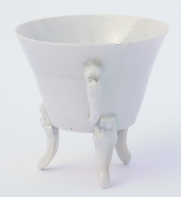 An 18thC Qing dynasty blanc-de-chine porcelain libation cup, of twin handed, tapering form, raised on three mask capped, scroll feet, ex Royal Worcester Porcelain Works Museum label, inventory number 8978, 7cm high. (AF) - 2