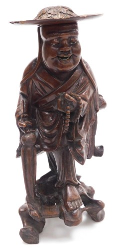 A late 19thC Qing dynasty hardwood carving of a priest, modelled standing, holding a string of beads, and a parasol, with a foliate carved hat, 35cm high.