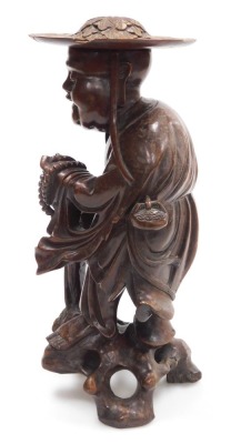 A late 19thC Qing dynasty hardwood carving of a priest, modelled standing, holding a string of beads, and a parasol, with a foliate carved hat, 35cm high. - 2