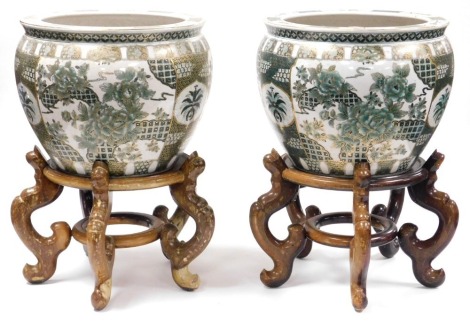 A pair of late 20thC Chinese famille verte fish bowls, decorated with reserves of flowers, gilt heightened, raised on wooden stands, 36cm wide, 56cm high all in.