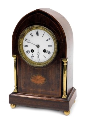 An Edwardian mahogany lancet cased mantel clock, circular enamel dial bearing Roman numerals, eight day movement with bell strike, the case with paterae and line inlay, raised on brass columns, and a rectangular base, on brass ball feet, with pendulum and