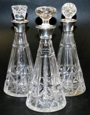 A set of three George VI cut glass decanters, of outswept form, with unmatched stoppers, and silver collars, London 1938, 31cm high.