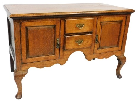 A Georgian style oak dresser base, with two short drawers flanked by a pair of cupboard doors, raised on cabriole legs, 78cm high, 121cm wide, 60cm deep.