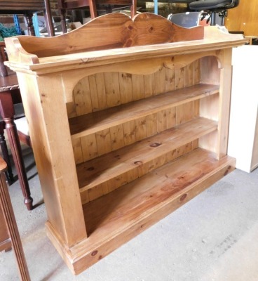 A pine open bookcase, the raised back above three central shelves, on a plinth base, 114cm high, 130cm wide, 37cm deep.