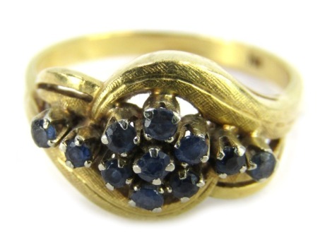 A sapphire dress ring, the central floral cluster flanked by four outer sapphires, in a twist and hammered design setting, yellow metal stamped 18kt, ring size P½, 5.3g all in.