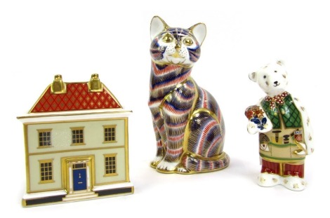 A group of Royal Crown Derby porcelain, comprising Derby cat paperweight, lacking stopper, 13cm high, Teddy Bear paperweight holding a bunch of flowers, seconds, 10cm high, and a Derby house paperweight, seconds, 9cm high. (3)