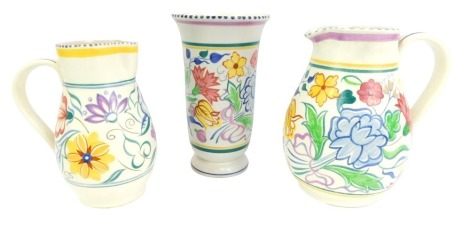 Three items of Poole pottery, traditionally decorated with floral sprays, comprising two jugs, 20cm high and 18.5cm high, and a vase, 21cm high.