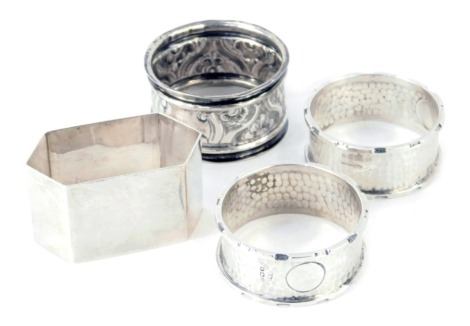 Four George V and later silver napkin rings, comprising a pair of hammered rings with vacant cartouche, a hexagonal ring and another with floral embossed central decoration, Birmingham assay, 2.49oz. (4)