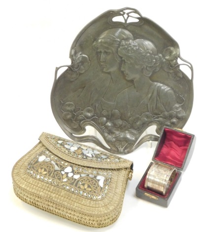 An early 20thC Continental Art Nouveau pewter dish, relief moulded with two female figures amongst flowers, No 223, 21cm wide (AF), together with an Eastern brass and mother of pearl inlaid evening bag, 17cm wide, a silver napkin ring in leather box.