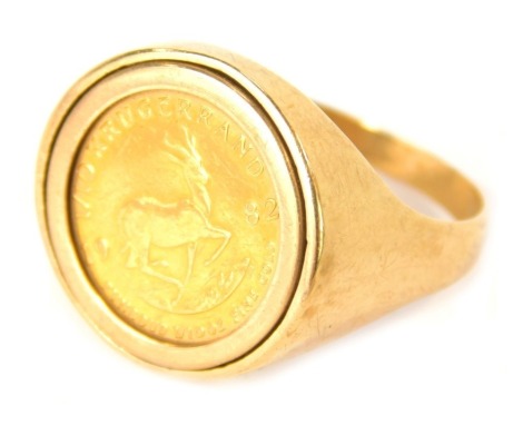 A 9ct gold 1/10th of a krugerrand ring, set with a 1982 1/10 of a krugerrand coin, in a clip setting, on a plain band, size V½, 8.1g all in.