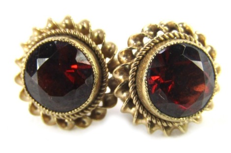 A pair of 9ct gold garnet studs, each in rub over setting, with twist borders on single pin with butterfly backs, 1.7g all in.