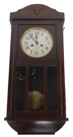 A mid 20thC oak cased drop dial wall clock, with circular silvered dial bearing Arabic numerals, eight day movement with coil strike, the case with a carved pediment and triple bevelled panelled glass door, 80cm high, 32cm wide, 18cm deep.