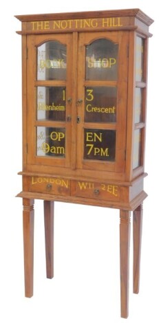 A 20thC oak cabinet on stand, the moulded top above writing for The Notting Hill Bookshop, with two panelled glazed doors and sides enclosing three shelves, the base with two frieze drawers, on square tapering legs, 151cm high, 64cm wide, 32cm deep.