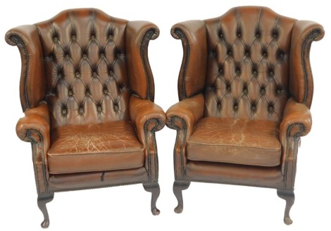 A pair of brown leather wing back armchairs, with button back, stud work and moveable seat, on mahogany pad feet. The upholstery in this lot does not comply with the 1988 (Fire & Fire Furnishing) Regulations, unless sold to a known exporter or upholsterer