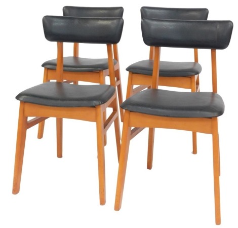 A set of four 1970s Schrieber teak dining chairs, each with a black leatherette padded seat and back, with square tapering legs untied by stretchers. The upholstery in this lot does not comply with the 1988 (Fire & Fire Furnishing) Regulations, unless s