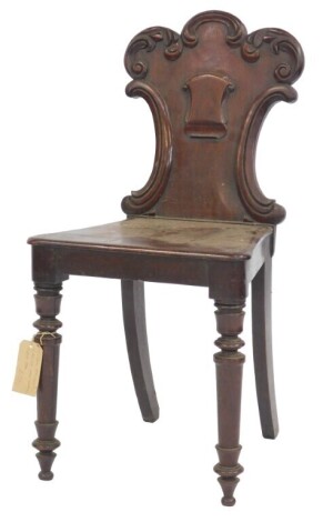 A Victorian mahogany hall chair, the solid carved back with shield crest and scroll motifs, with a solid seat, on turned tapering legs.