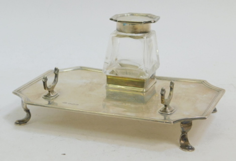 A George V silver and cut glass desk stand, of canted rectangular form, with a cut glass inkwell, with silver mount and hinged lid, raised on four paw feet, presentation engraved, Sheffield 1919, 4.88oz.