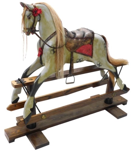 A dapple grey painted rocking horse, with leather saddle and bridle, etc., on an ash trestle base with turned supports, 128cm high, 150cm long.